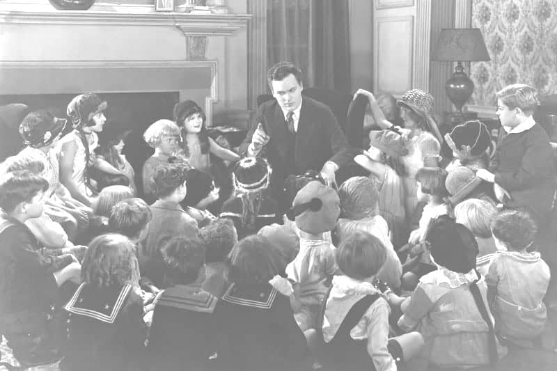 black and white photo of man telling a story to a large group of spellbound children