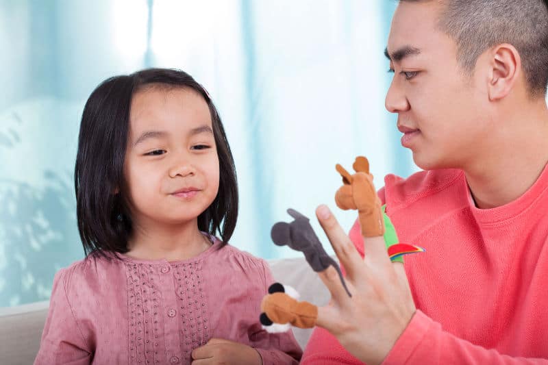 Asian girl with male teacher using finger puppets
