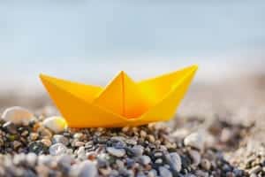 origami of yellow boat on pebbles
