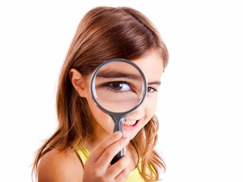 middle school age girl playing detective with a giant magnifying glass
